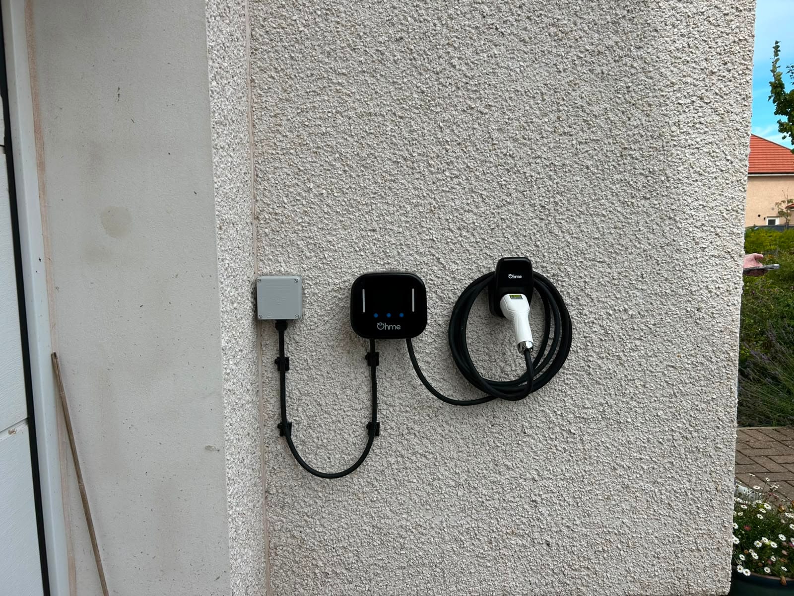 Ohme Home Pro EV charger installed on an exterior wall, with its cable coiled on a wall-mounted holder