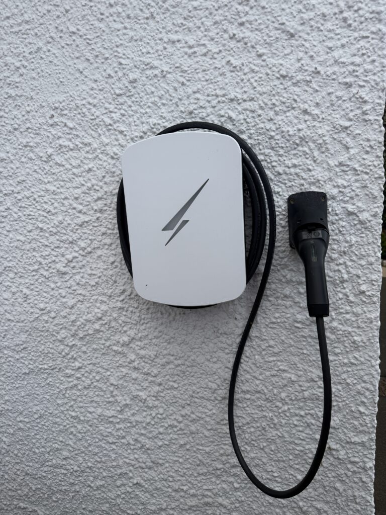 White Hypervolt Home 3 Pro EV charger installed on an exterior wall in Colinton, Edinburgh, with its charging cable and wall-mounted connector holder