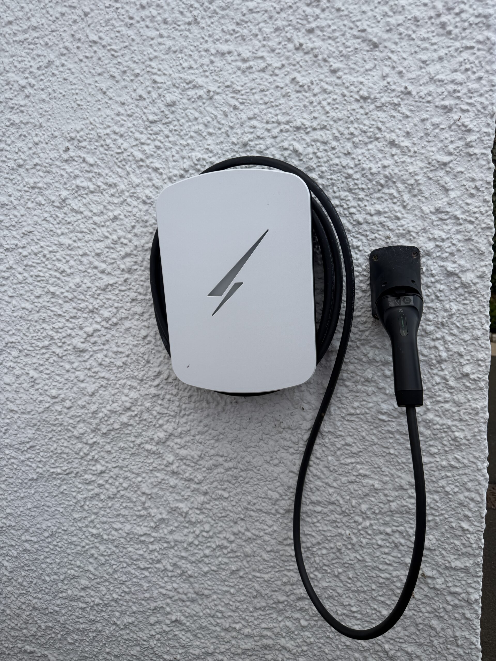 White Hypervolt Home 3 Pro EV charger installed on an exterior wall in Colinton, Edinburgh, with its charging cable and wall-mounted connector holder
