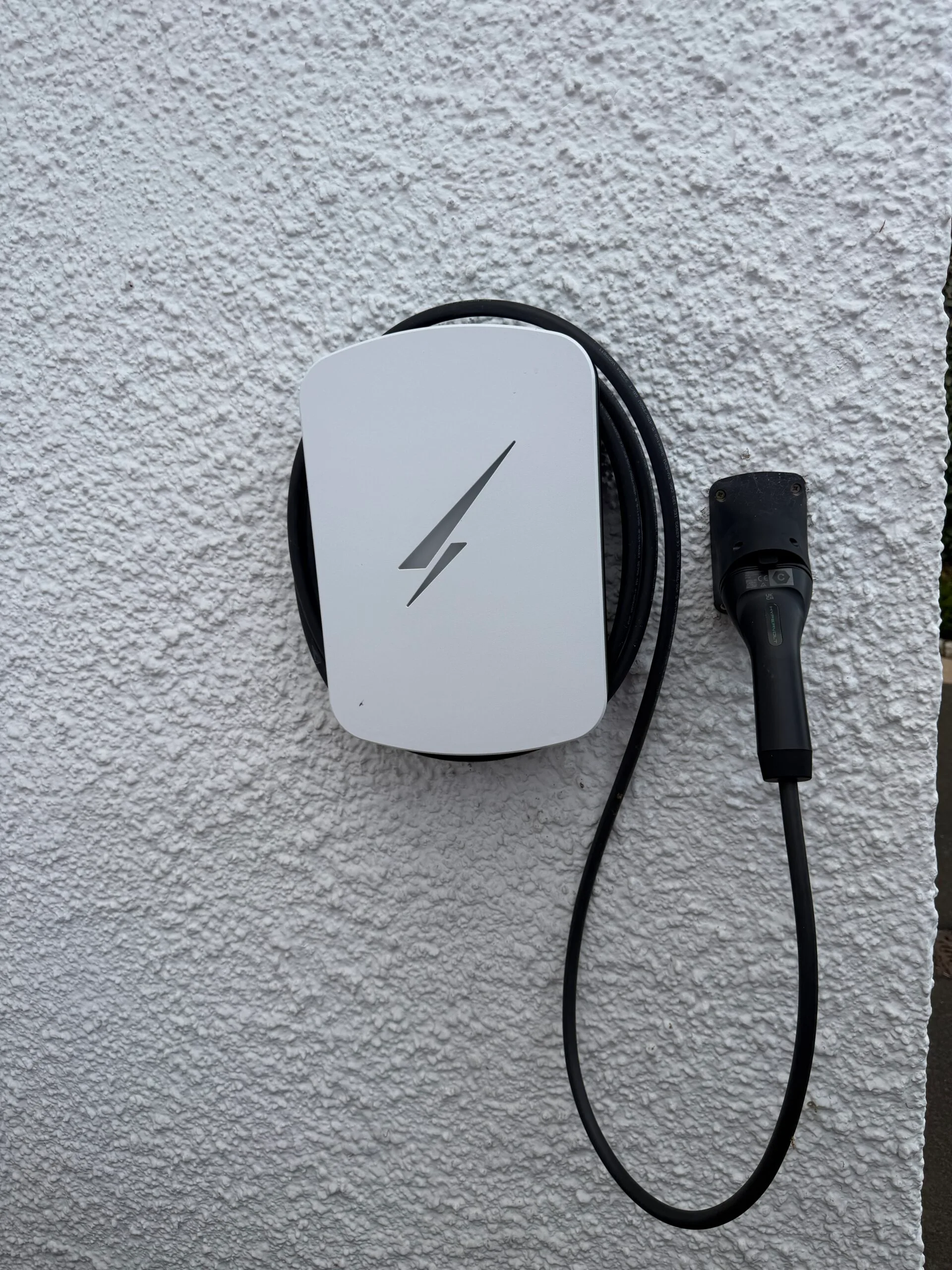 White Hypervolt Home 3 Pro EV charger installed on an exterior wall in Colinton, Edinburgh, with its charging cable and wall-mounted connector holder