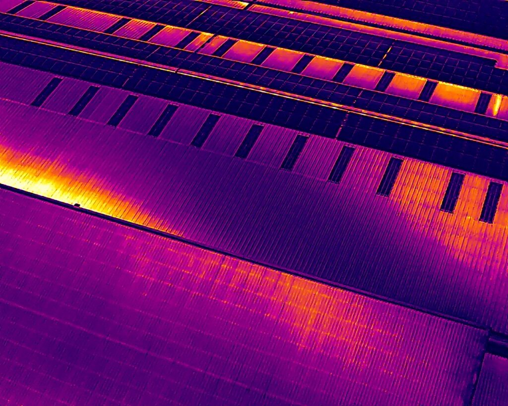 Drone thermal image showing rows of commercial solar PV modules and the surrounding roof