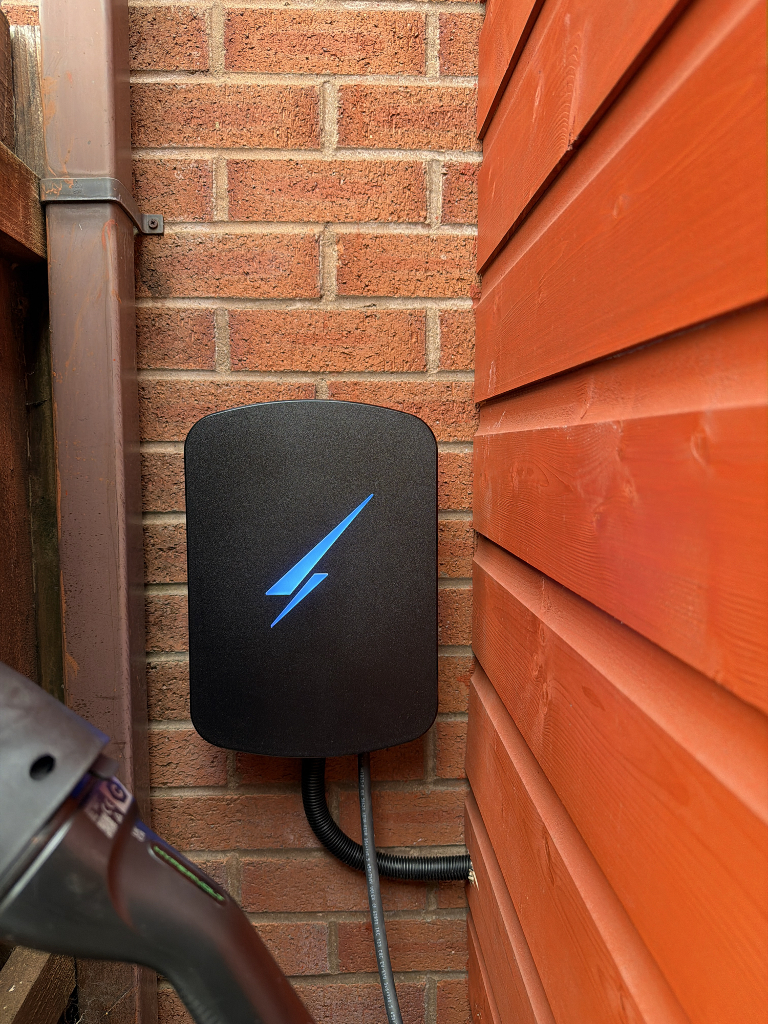 Black Hypervolt Home 3 Pro EV charger with illuminated blue logo mounted on an exterior brick wall in Bonnyrigg.